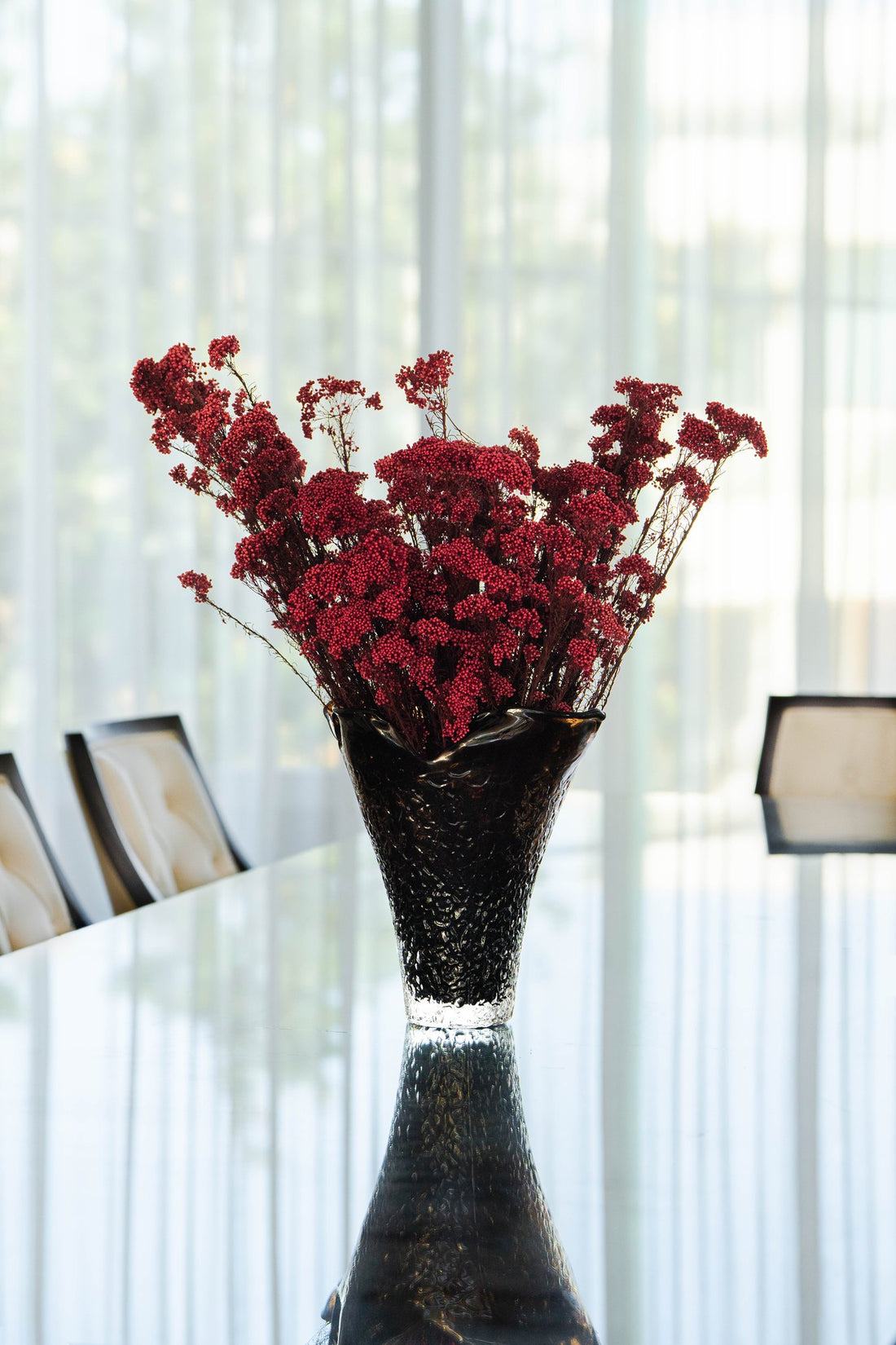 RUBY deep red preserved rice flower en masse in Lashay tall vessel amber by The Palmier, on a dining table